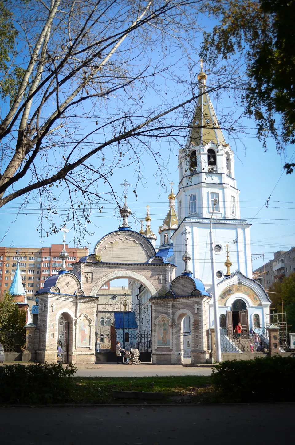 Кирпичная шатровая колокольня и купол храма на фоне неба, деревья на переднем плане